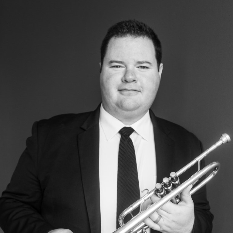 Man in a suit holding a trumpet in both hands.