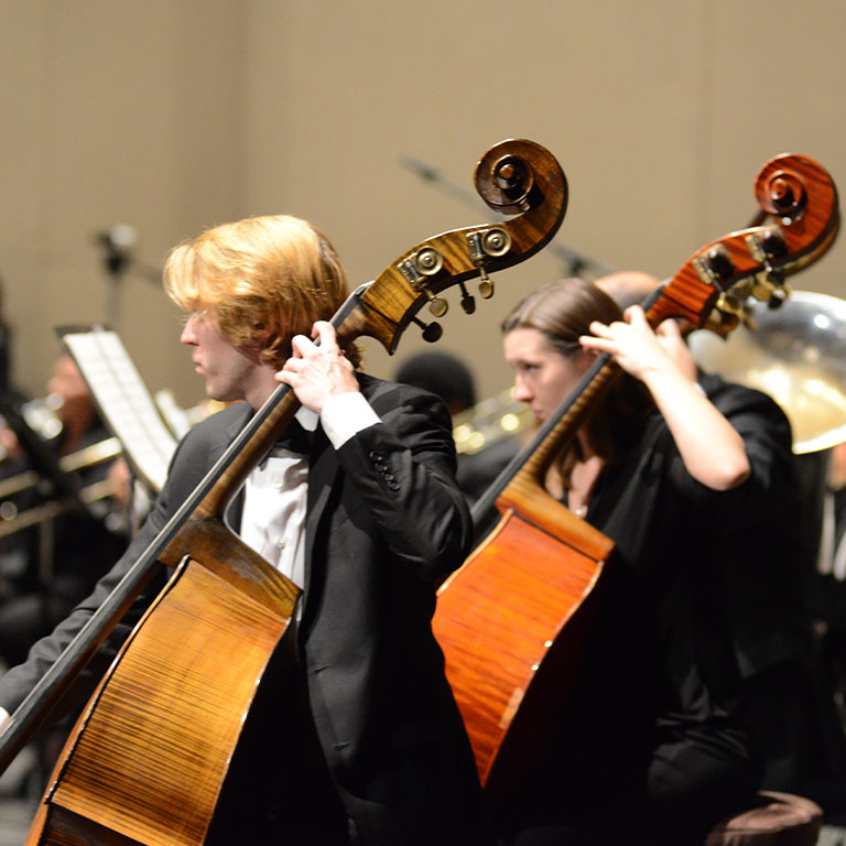 Two standing bass players performing on the Musical Arts Center stage.