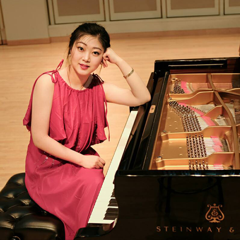 woman in a pink dress, posed and seated at a piano