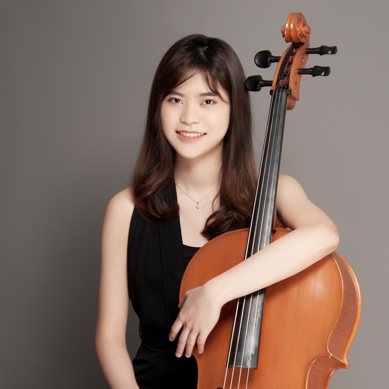 Woman wearing a black dress, smiling with her left arm wrapped around the neck of a cello
